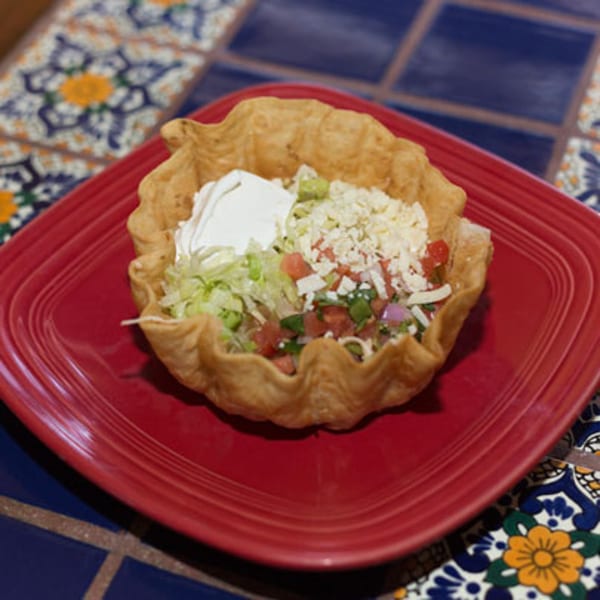 A taco salad in a crispy tortilla bowl with lettuce, pico de gallo, cheese, and sour cream.