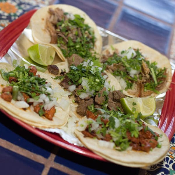 A red plate of Los Cocos Mexican Restaurant tacos with various fillings, cilantro, onions, and lime.