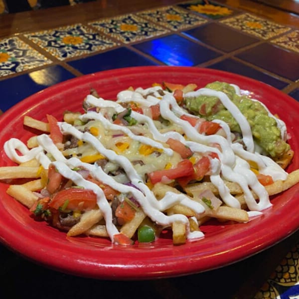 Loaded fries with melted cheese, diced tomatoes, sour cream, and guacamole on a red plate.