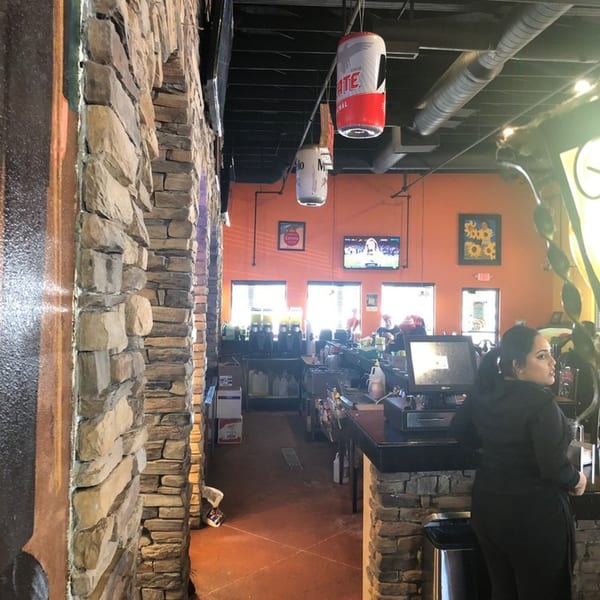 Interior of Los Cocos Mexican Restaurant with stone walls, orange accents, and a bar area.