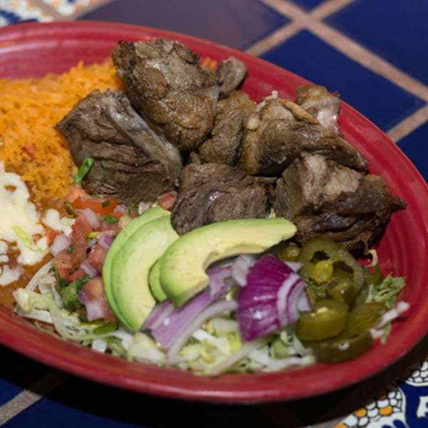 A red plate of Mexican food with chunks of meat, rice, beans, avocado, and pickled jalapeños.
