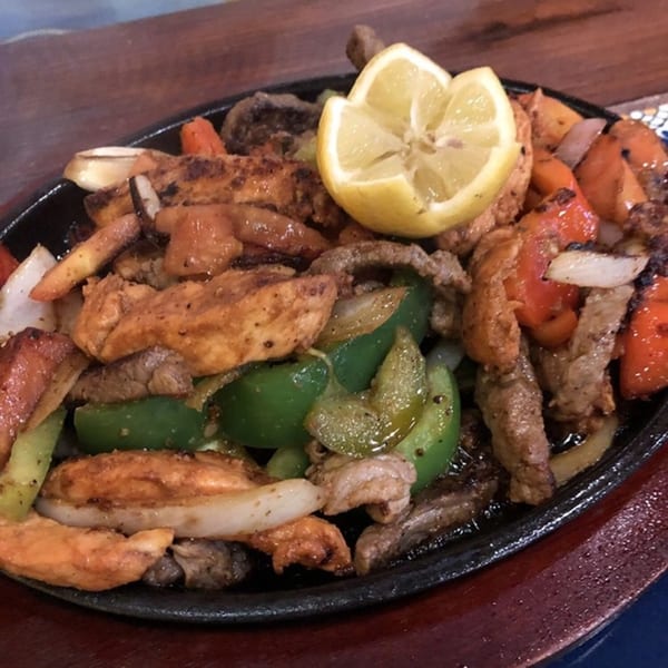 Sizzling Los Cocos fajitas with chicken, beef, peppers, onions, and a lemon wedge.