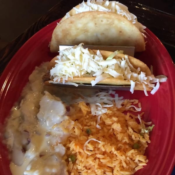Three tacos with shredded cheese, rice, and beans on a red plate at Los Cocos Mexican Restaurant.