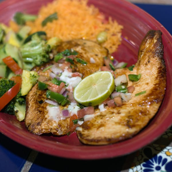 Grilled chicken with pico de gallo, lime, rice, and mixed vegetables on a red plate.