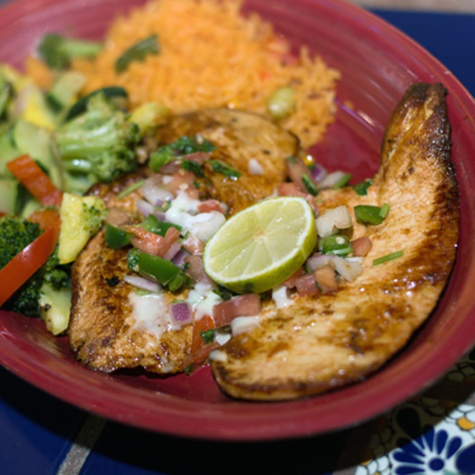 Grilled chicken with pico de gallo, lime, rice, and mixed vegetables on a red plate.