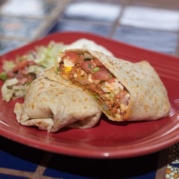 A large, cut burrito filled with meat, cheese, and vegetables, served with a side salad.