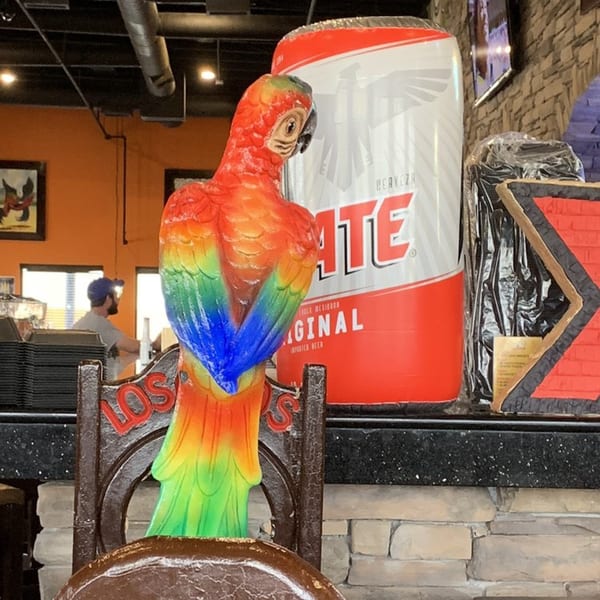 A colorful parrot statue and a large Tecate beer can display at Los Cocos Mexican Restaurant.