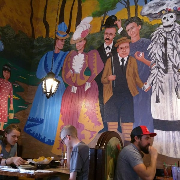 A vibrant mural of people in traditional Mexican attire and a skeleton adorns the restaurant wall.