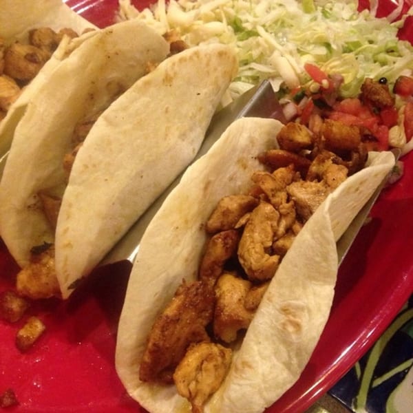 Three chicken tacos with shredded lettuce and pico de gallo on a red plate.