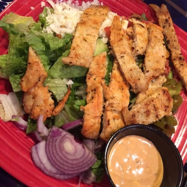 Grilled chicken strips on a bed of lettuce with shredded cheese, red onions, and a side of dressing.