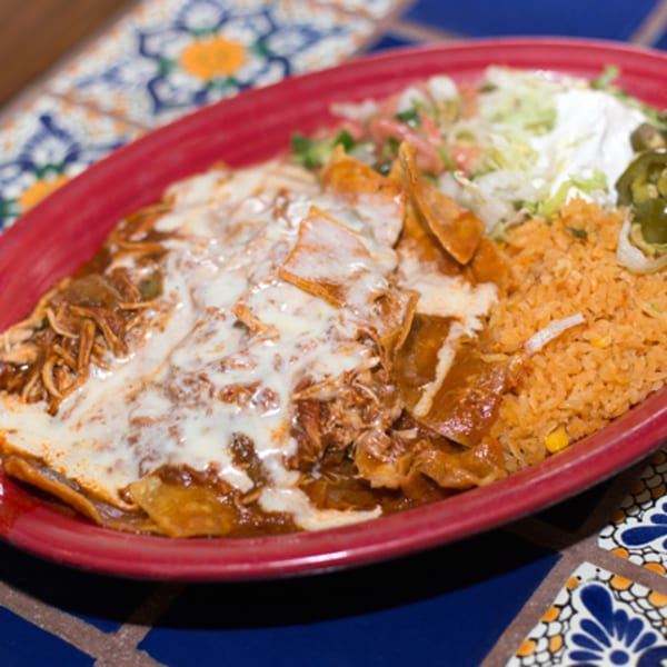 A red plate of Los Cocos Mexican chilaquiles with rice, lettuce, sour cream, and jalapeños.