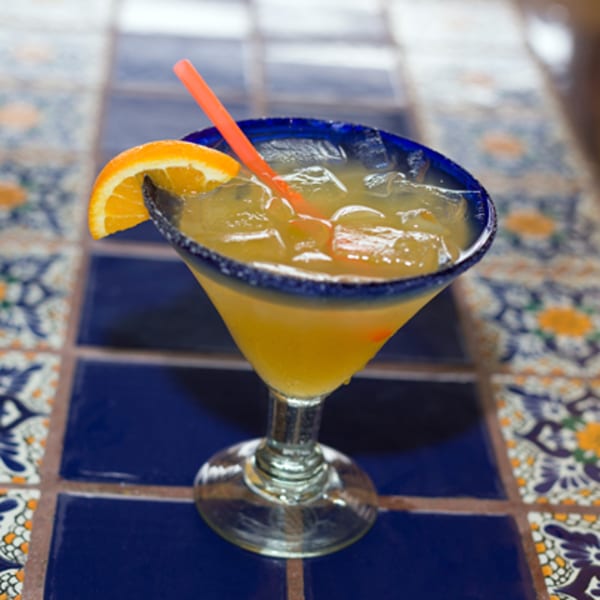 Margarita with orange slice and straw in a blue-rimmed glass on a colorful tiled table.